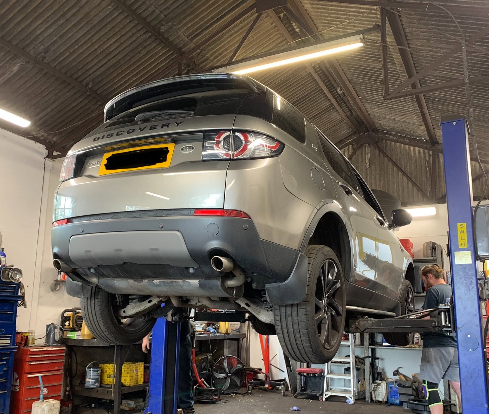 A Land Rover Discovery Sport up on the lift in our workshop with a technician working underneath