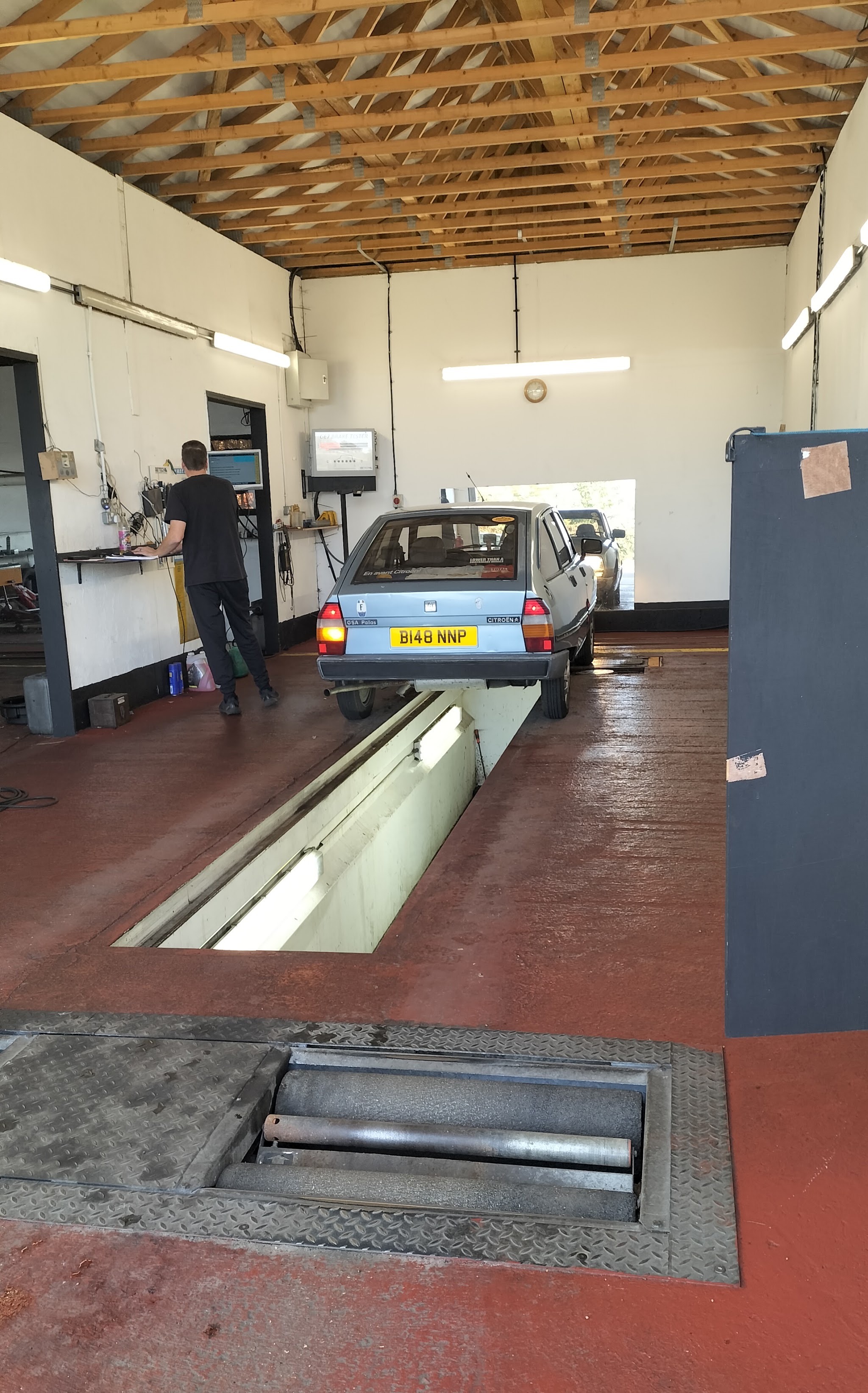 Inside our MOT bay: a classic Citroën on the test lane with the brake rollers in the foreground and the tester at the computer